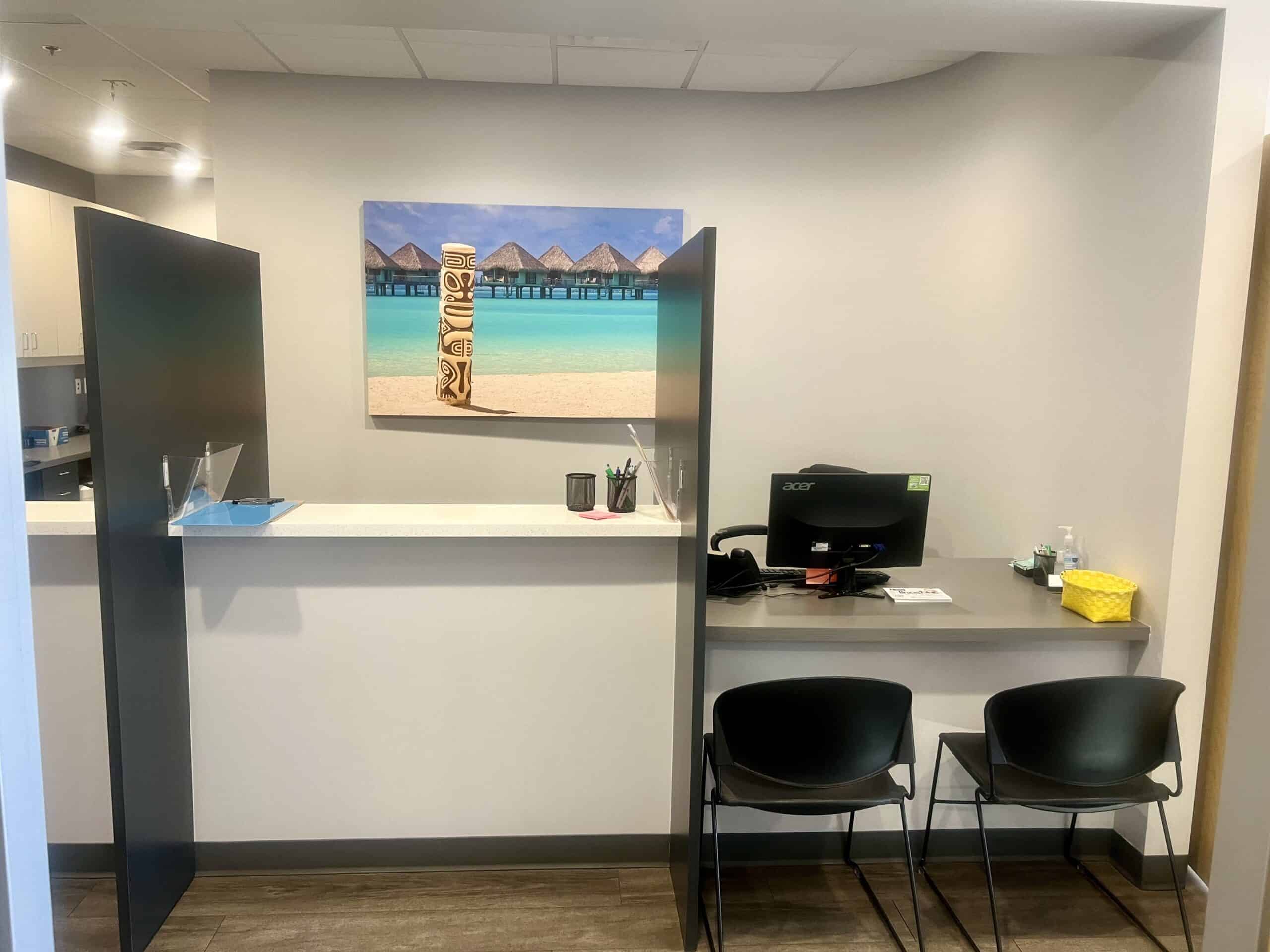 A welcoming pediatric dental office reception desk with seating, tropical beach art, and supplies.